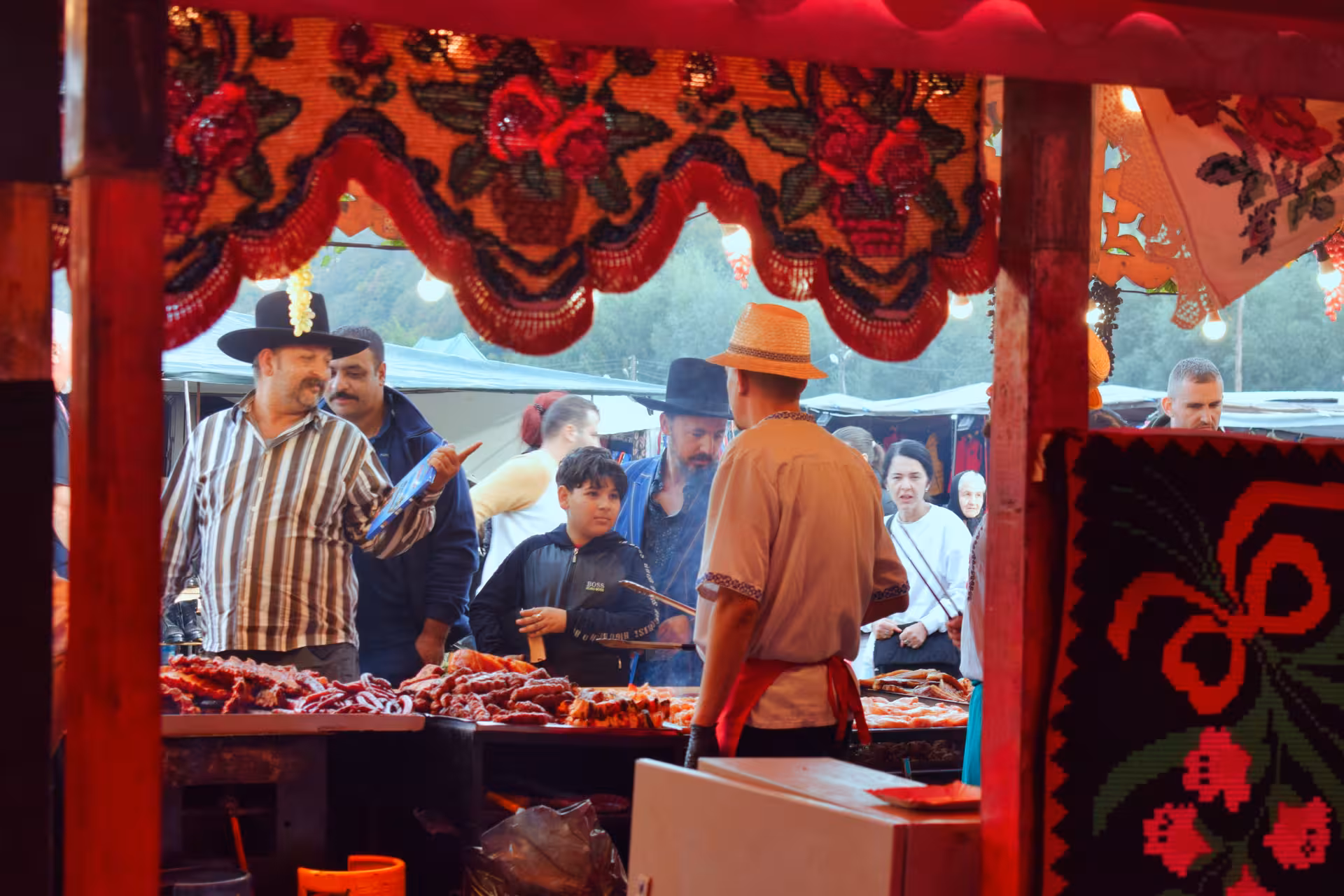 Lively food stall at Negreni Flea Market with locals in traditional hats browsing grilled meats under colorful handmade canopy