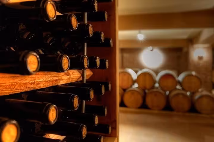 Wine cellar rack with bottles and oak barrels, showcasing Nemea winery aging on Greece Wine Roads tour