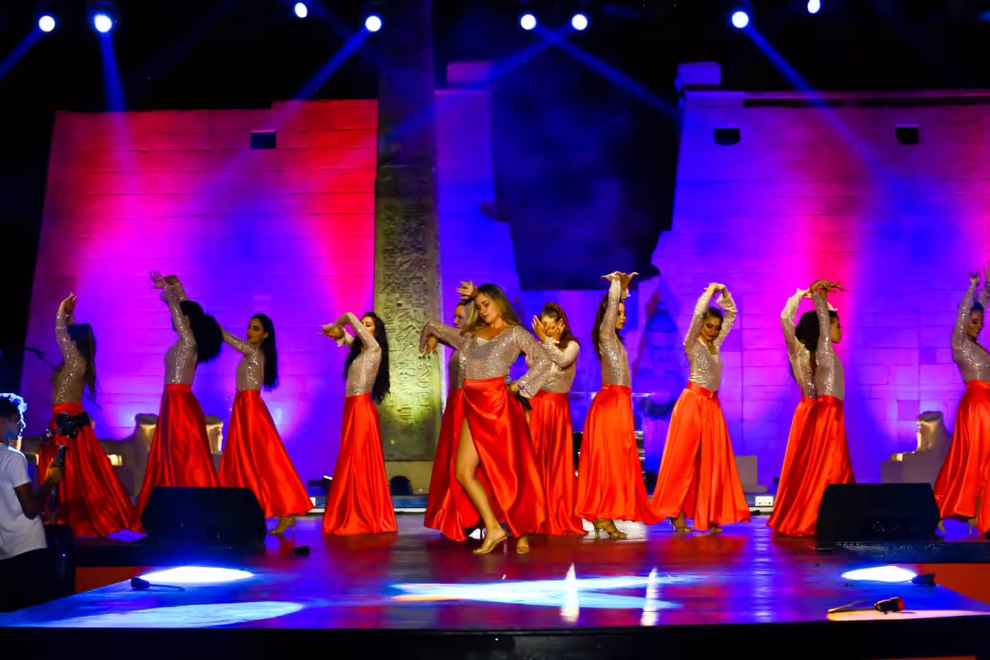 Dancers in red skirts perform choreography at Neverland Musical and Cabaret Show under vibrant purple lighting