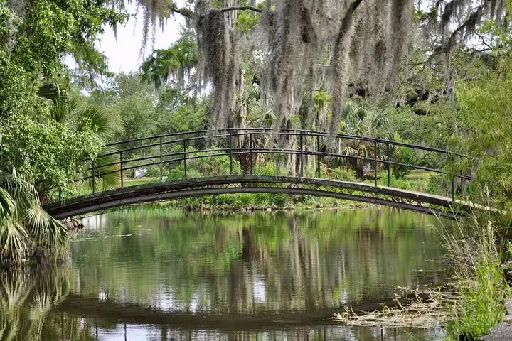 Arched iron footbridge over a tranquil pond surrounded by Spanish moss-draped trees in New Orleans City Park