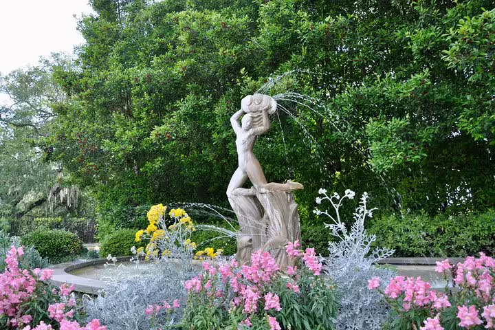 Stone fountain statue surrounded by pink and yellow flowers in New Orleans City Park gardens