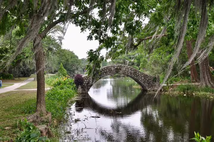 Stone arch bridge over calm bayou surrounded by oak trees draped in Spanish moss in New Orleans City Park