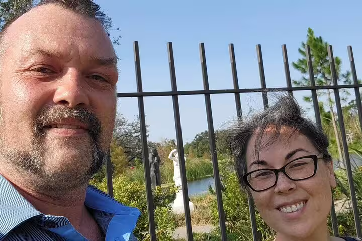 Couple taking selfie at iron fence in New Orleans City Park with garden statues and pond behind them