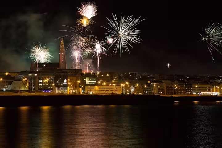 Colorful New Year fireworks bursting over Reykjavik city skyline reflected in harbor waters at night