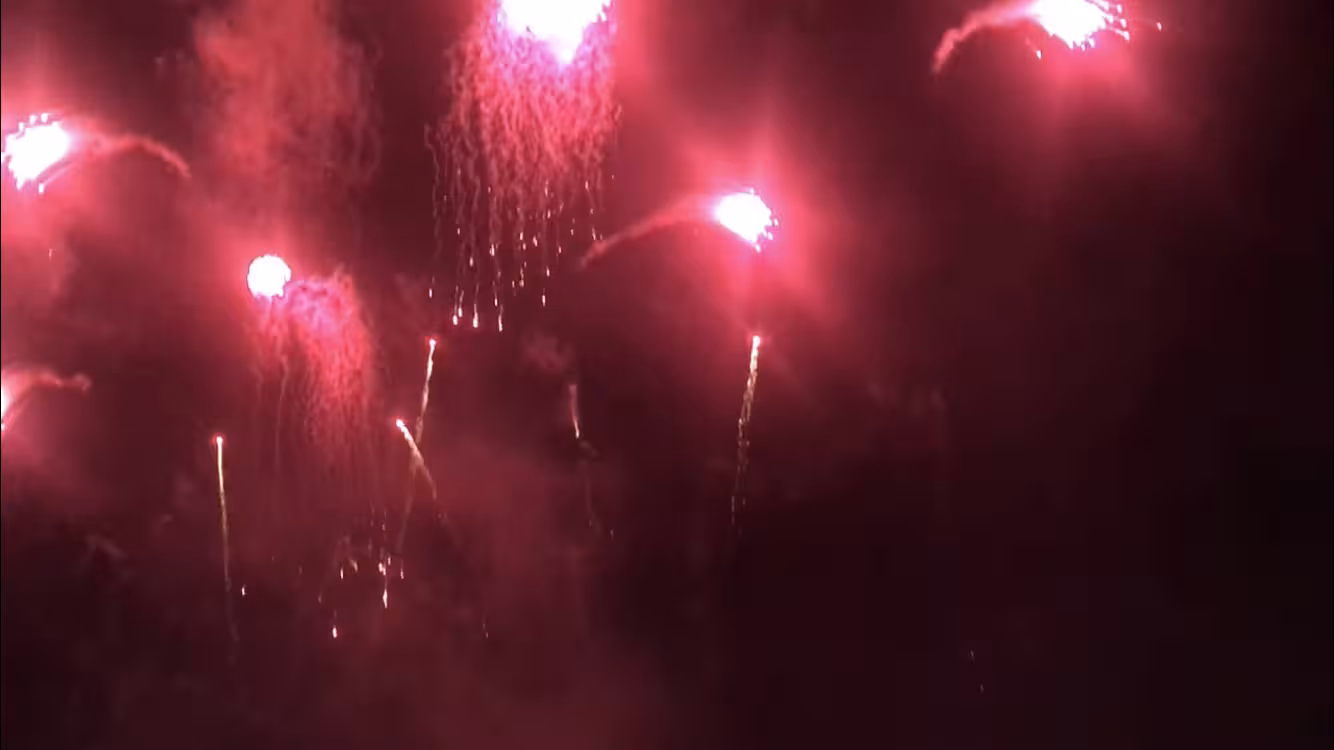 Red fireworks lighting the night sky during a New Year’s Eve sailboat cruise, festive midnight countdown view