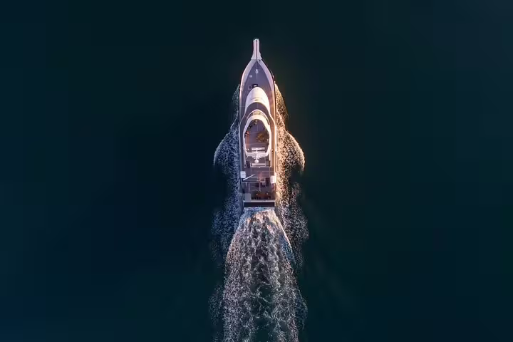 Aerial view of luxury yacht cruising at night leaving white wake trail on dark water