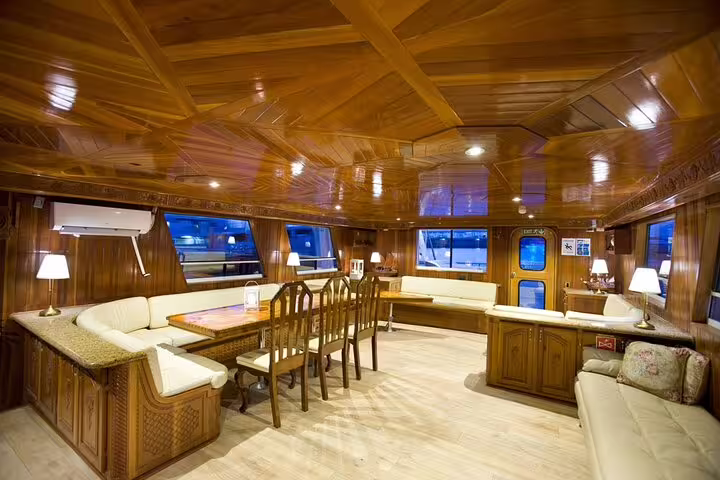 Elegant wooden interior saloon of a luxury yacht with cream seating, dining table, and panoramic windows at night