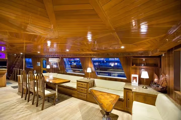 Luxury wooden interior of a yacht salon with seating, lamps, and panoramic windows at night