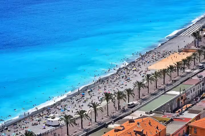 Aerial view of Nice beach promenade with turquoise Mediterranean Sea, palm trees, and sunbathers along the French Riviera