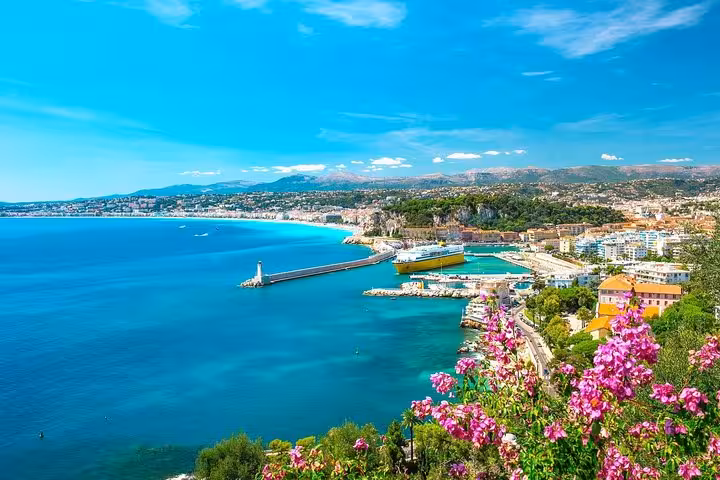 Panoramic view of Nice coastline with turquoise Mediterranean sea, harbor, lighthouse, and pink flowers in foreground