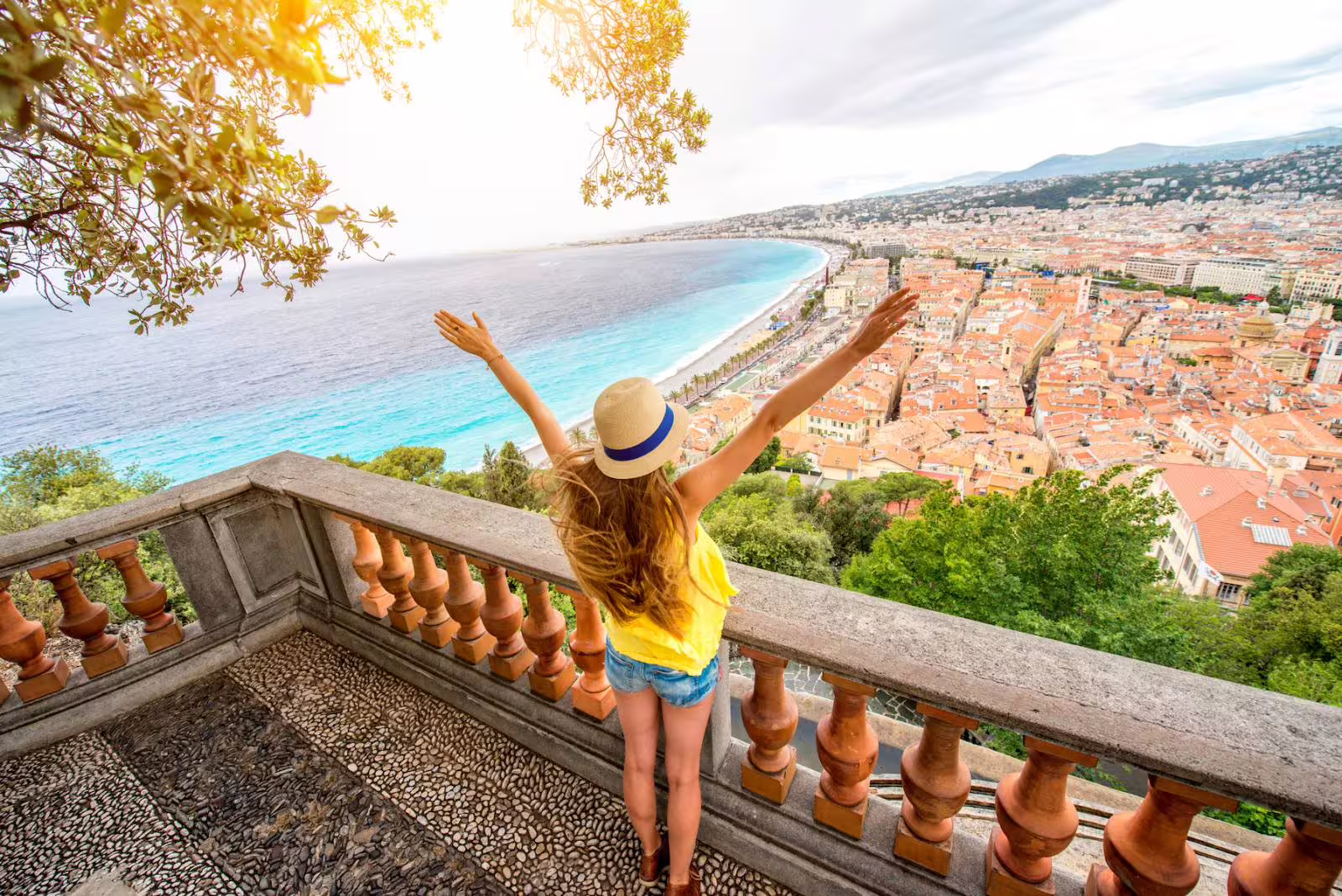 Woman with arms raised overlooking Nice's turquoise coastline and terracotta rooftops from Castle Hill viewpoint