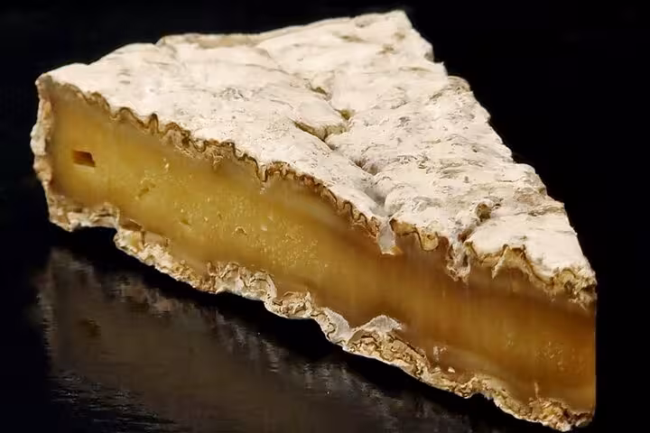 Wedge of aged French soft-rind cheese with white mold crust and golden interior on dark surface