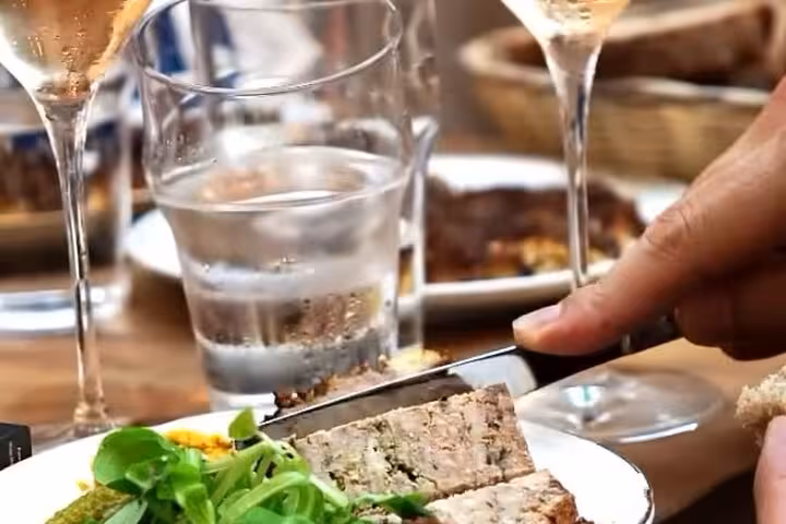 Hand slicing pâté on white plate with greens, wine glasses and water glass on restaurant table in Nice