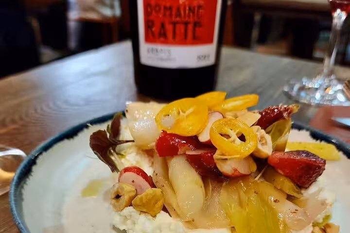 Fresh salad with radishes, yellow peppers and chicory beside a Domaine Ratte wine bottle in Nice