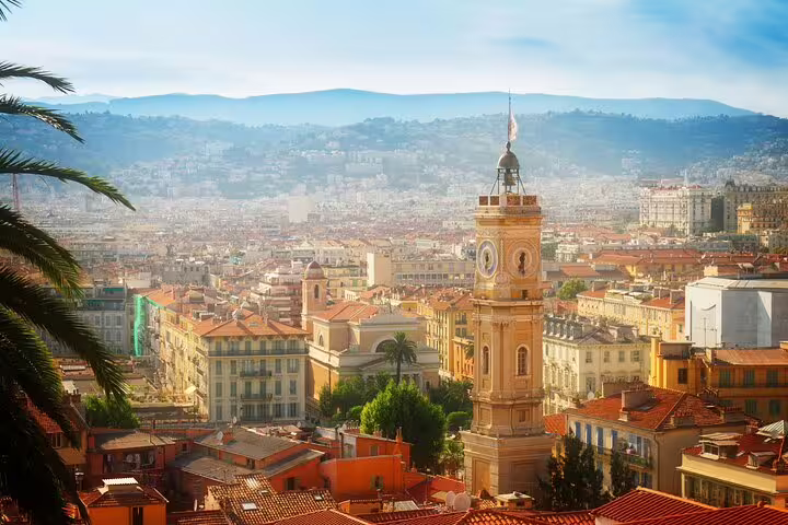 Aerial view of Nice old town with clock tower, terracotta rooftops, and mountains in background