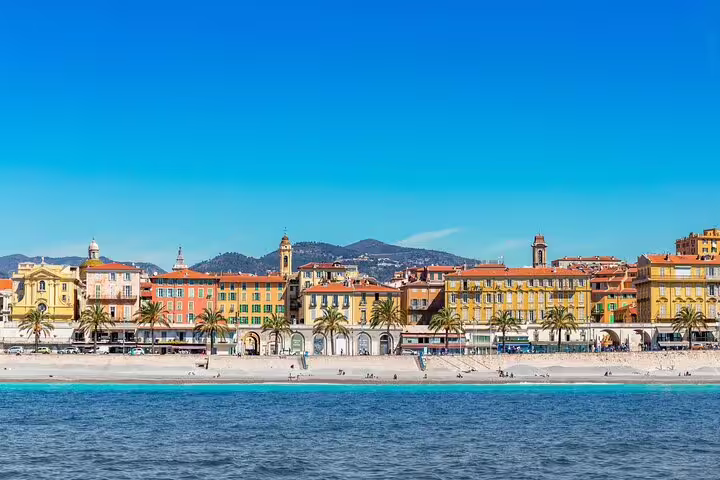 Colorful buildings and palm trees along Nice's beachfront promenade with turquoise Mediterranean waters