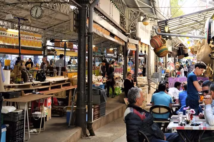 Busy outdoor market with shoppers and café diners under iron roof structure