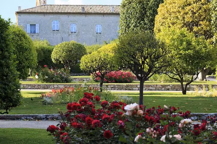 Formal French garden with red roses, manicured trees, and historic stone manor house in Nice region