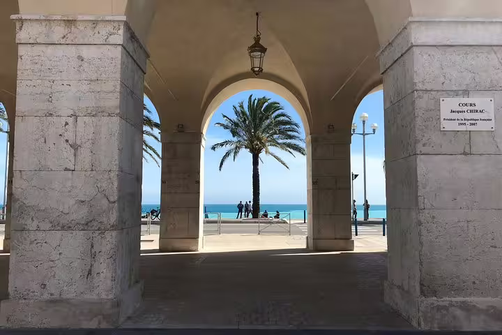 Arched colonnade framing a palm tree and turquoise Mediterranean sea at Nice Promenade des Anglais