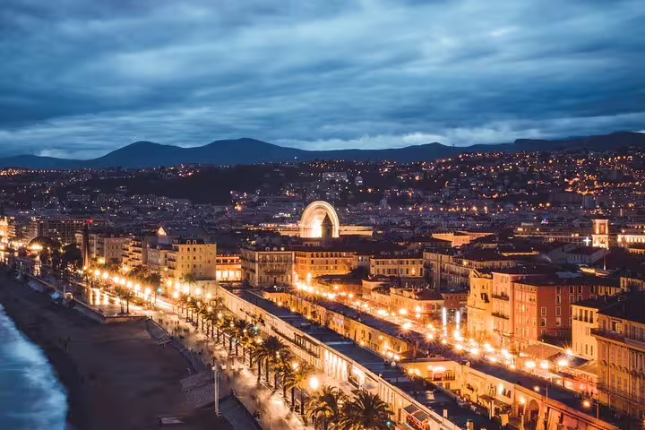 Aerial night view of Nice coastline promenade with city lights, Ferris wheel, and mountains in background