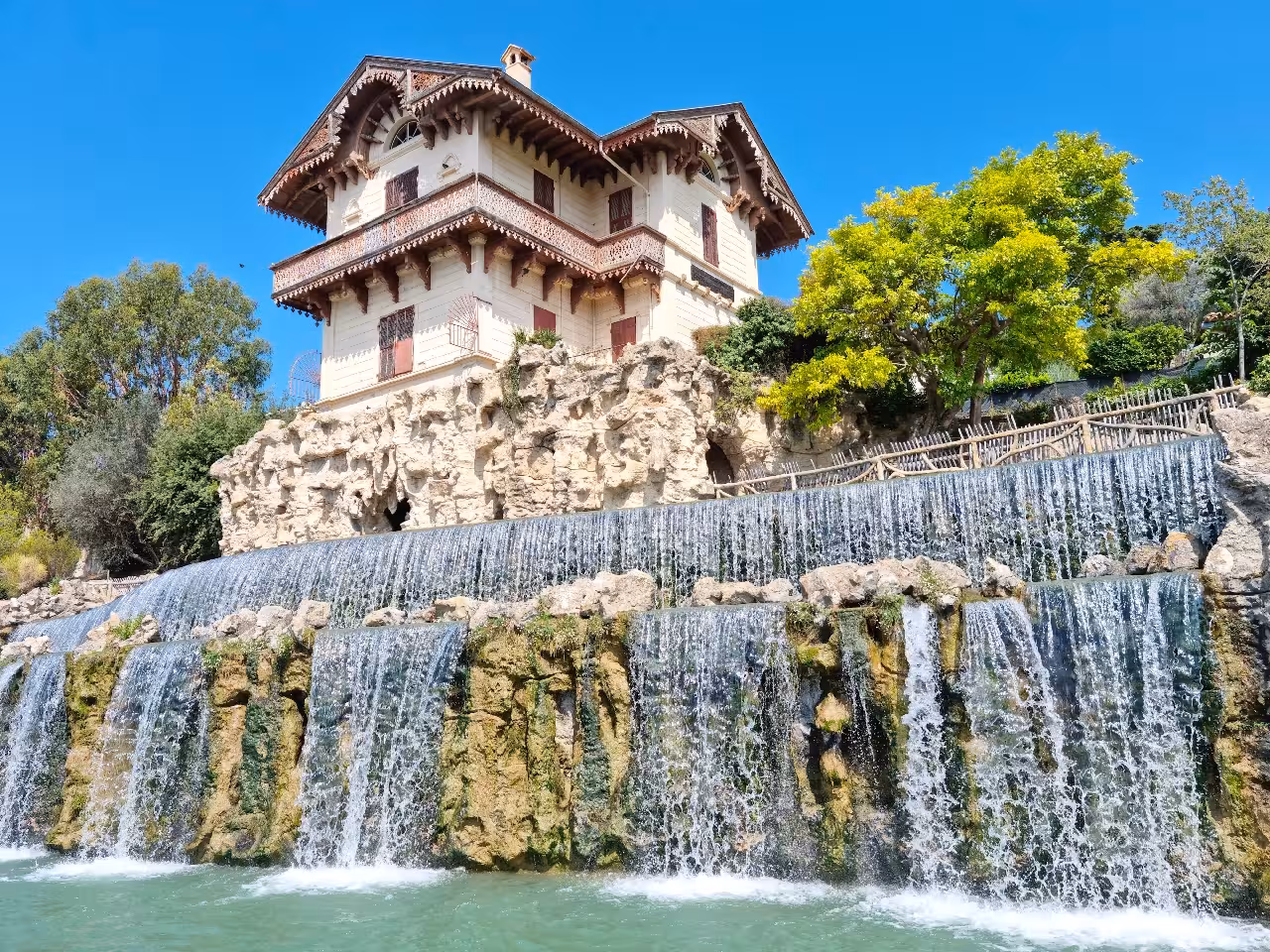 Ornate villa with cascading waterfalls over rocky cliffs surrounded by lush trees near Nice, France