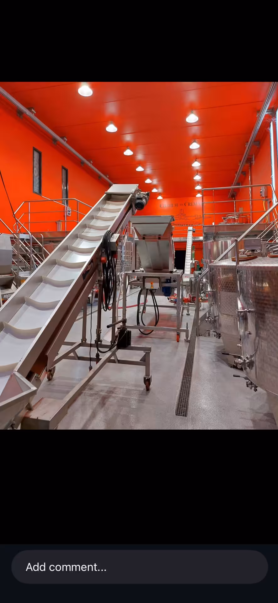 Stainless steel grape conveyor belt and fermentation tanks in red-walled winery facility
