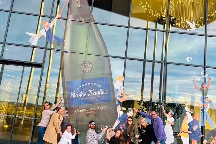 Small group posing by Nicolas Feuillatte champagne bottle mural in Reims, Champagne day tour from Paris