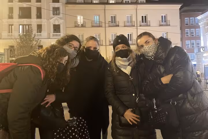 Group of five women wearing face masks posing together on a Madrid street at night