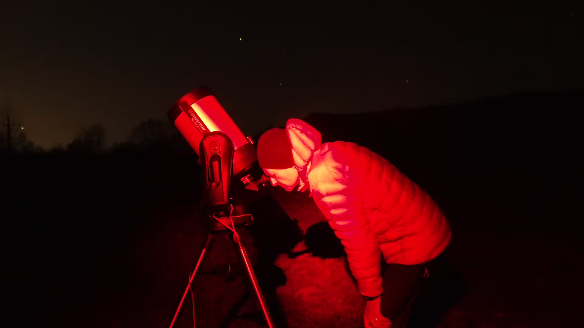Person in red jacket using Celestron telescope for stargazing at night in Romania
