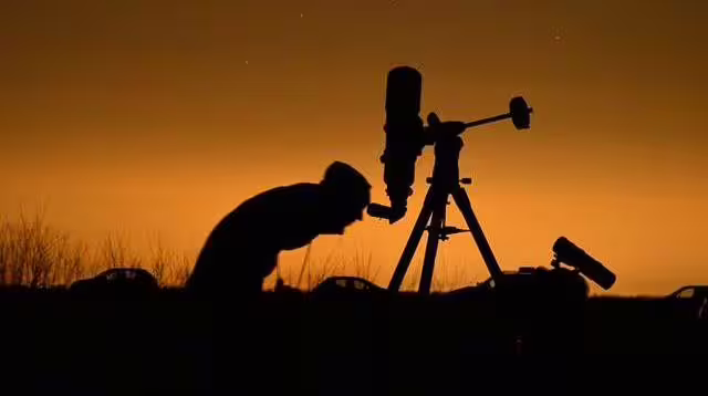 Silhouette of person looking through telescope at dusk during night sky stargazing tour in Romania