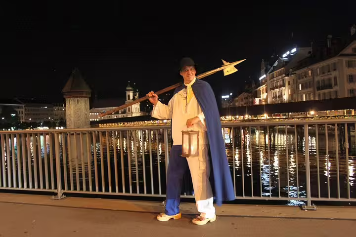 Nightwatchman in traditional attire holding a lantern on a Lucerne bridge, offering a glimpse into medieval Swiss history.