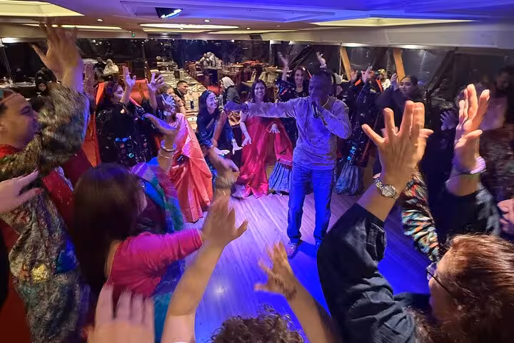 A joyful crowd participates in a lively dance performance during a Nile cruise dinner event.