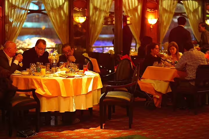 Guests dining in a warm-lit Nile Maxim dinner cruise cabin in Cairo before the belly dance and tannura show