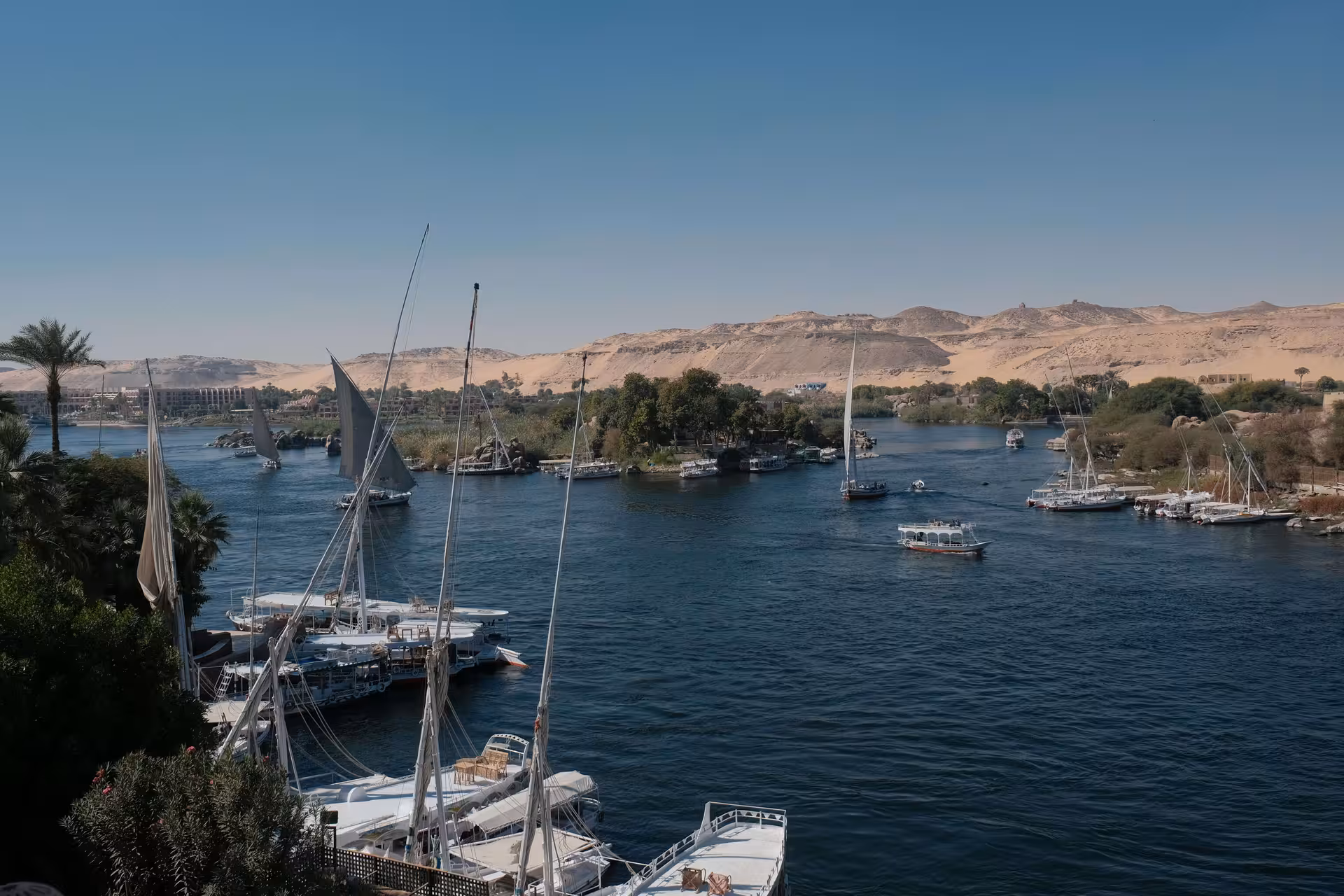 Felucca sailboats on the Nile River in Aswan with desert hills in the background