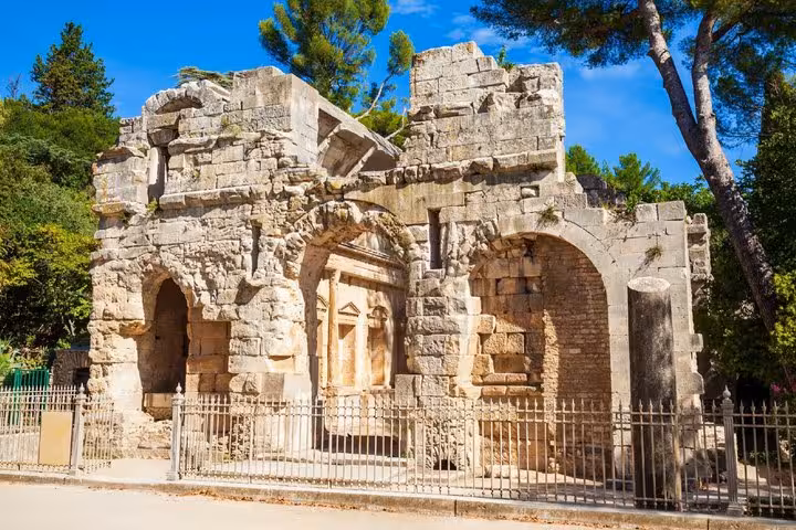 Ancient Roman ruins with arched stone walls surrounded by trees in Nimes, France