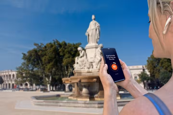 Tourist using GPS audio guide app on smartphone at Esplanade Charles de Gaulle fountain in Nimes