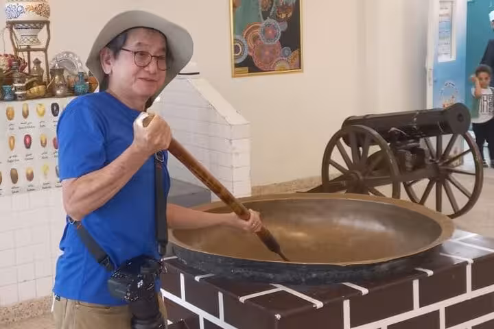 Visitor stirring a giant traditional copper pot inside Nizwa Fort museum during a cultural full-day group tour in Oman