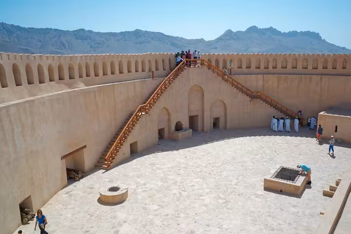 Visitors explore the sunlit courtyard and ramparts of historic Nizwa Fort on a guided full-day group tour in Oman