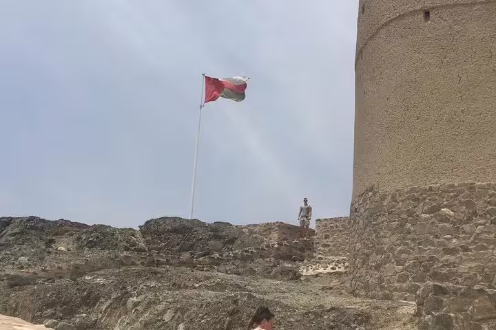 A person stands near the Oman flag at Nizwa Fort, illustrating the strong cultural heritage and scenic views of the fort.