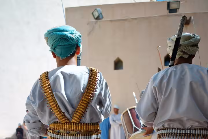 Traditional Omani performers in Nizwa Fort courtyard wearing ceremonial dress and ammunition belts on a cultural group tour