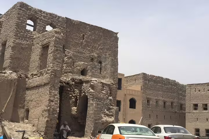 Historic ruins in Nizwa with ancient architecture, parked cars, and clear skies, capturing the essence of Oman.