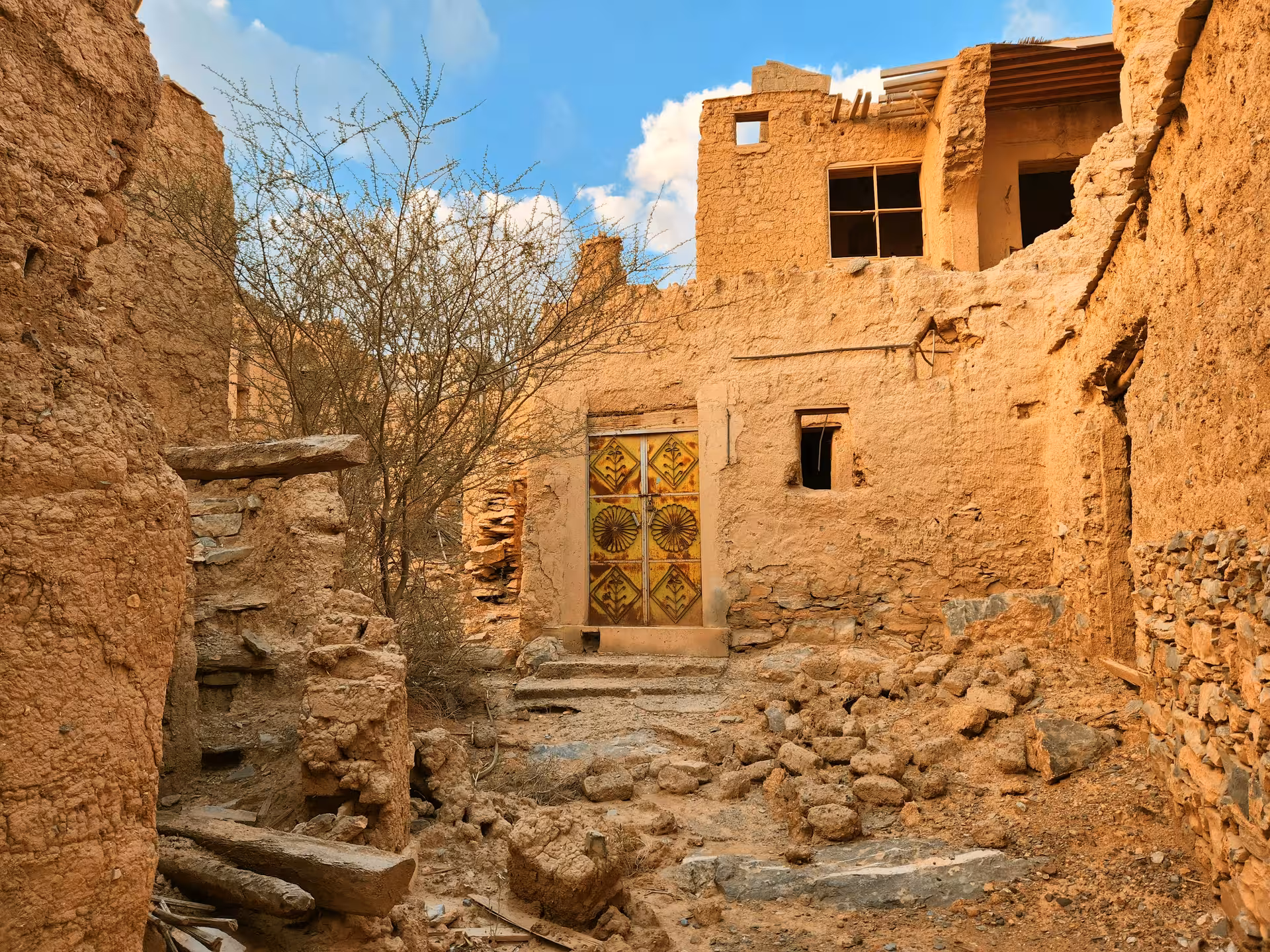 Abandoned mud-brick house with ornate wooden door in historic Nizwa village, explored on a Muscat cultural desert tour
