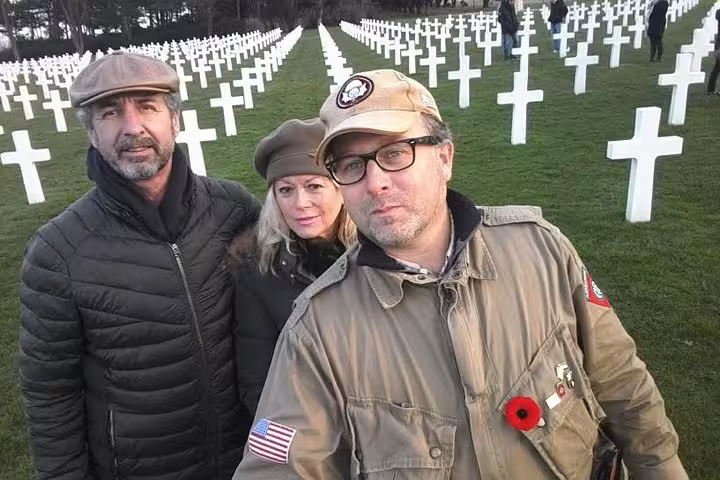 Three visitors posing at Normandy American Cemetery with rows of white crosses during D-Day beaches tour