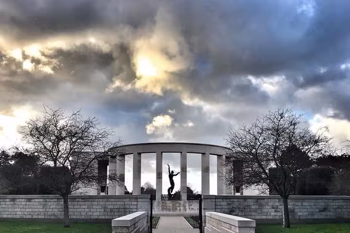 Normandy American Cemetery memorial colonnade with silhouetted statue under dramatic cloudy sky