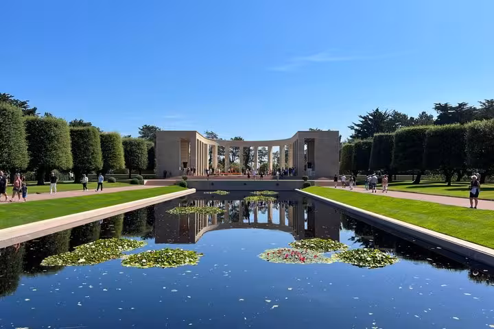 Reflection pool at Normandy American Cemetery memorial with colonnaded monument and manicured hedges on D-Day tour
