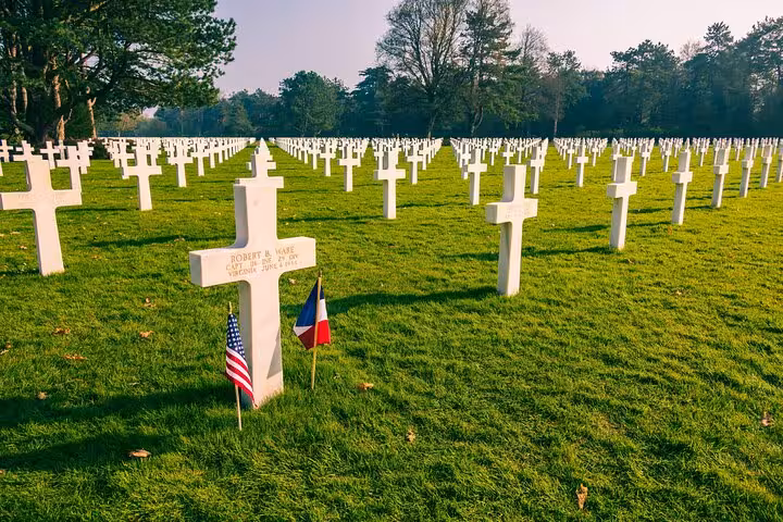 Rows of white crosses at Normandy American Cemetery with US and French flags at a gravestone