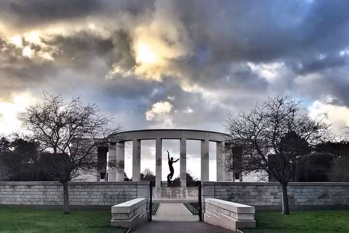 Normandy American Memorial colonnade with silhouetted figure statue under dramatic cloudy sky