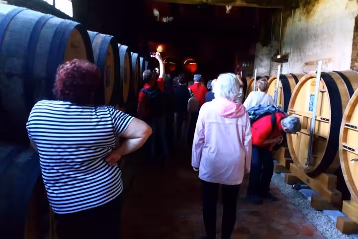 Tour group exploring a Normandy wine cellar with large oak barrels during a food and calvados tasting tour