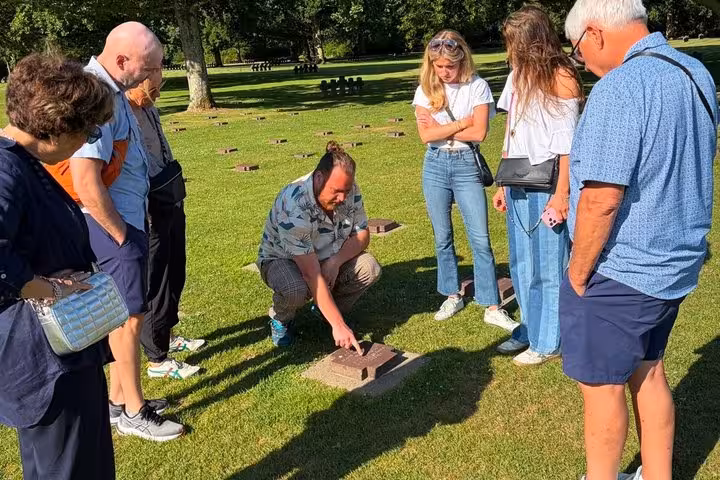 Tour guide pointing at grave marker at Normandy cemetery with group of visitors gathered around