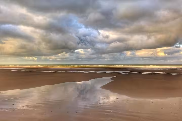 Wide sandy beach at low tide with dramatic cloudy sky reflected in shallow water pools, Normandy coast